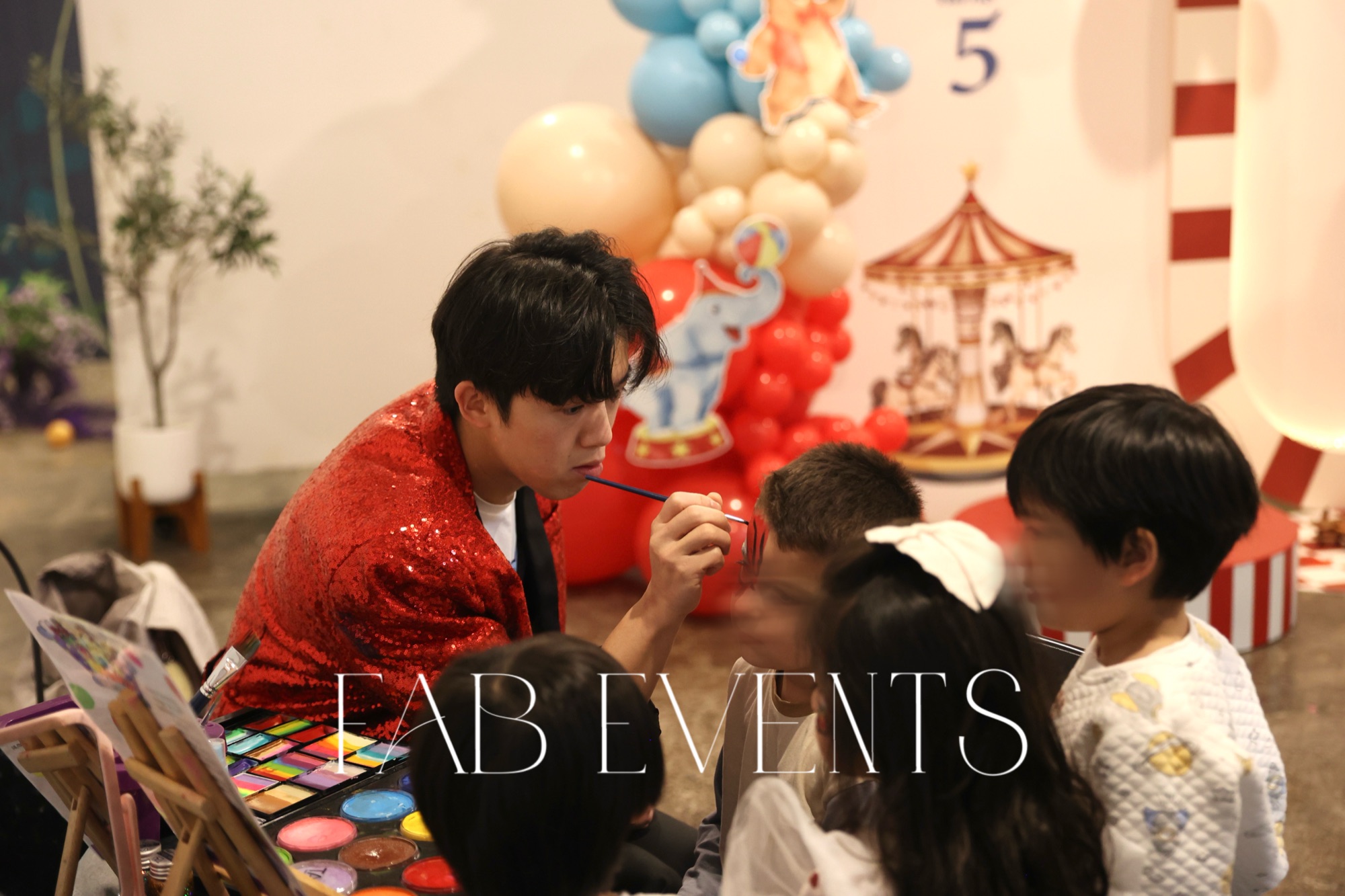 Face painting entertainer with children in front of a carousel birthday backdrop